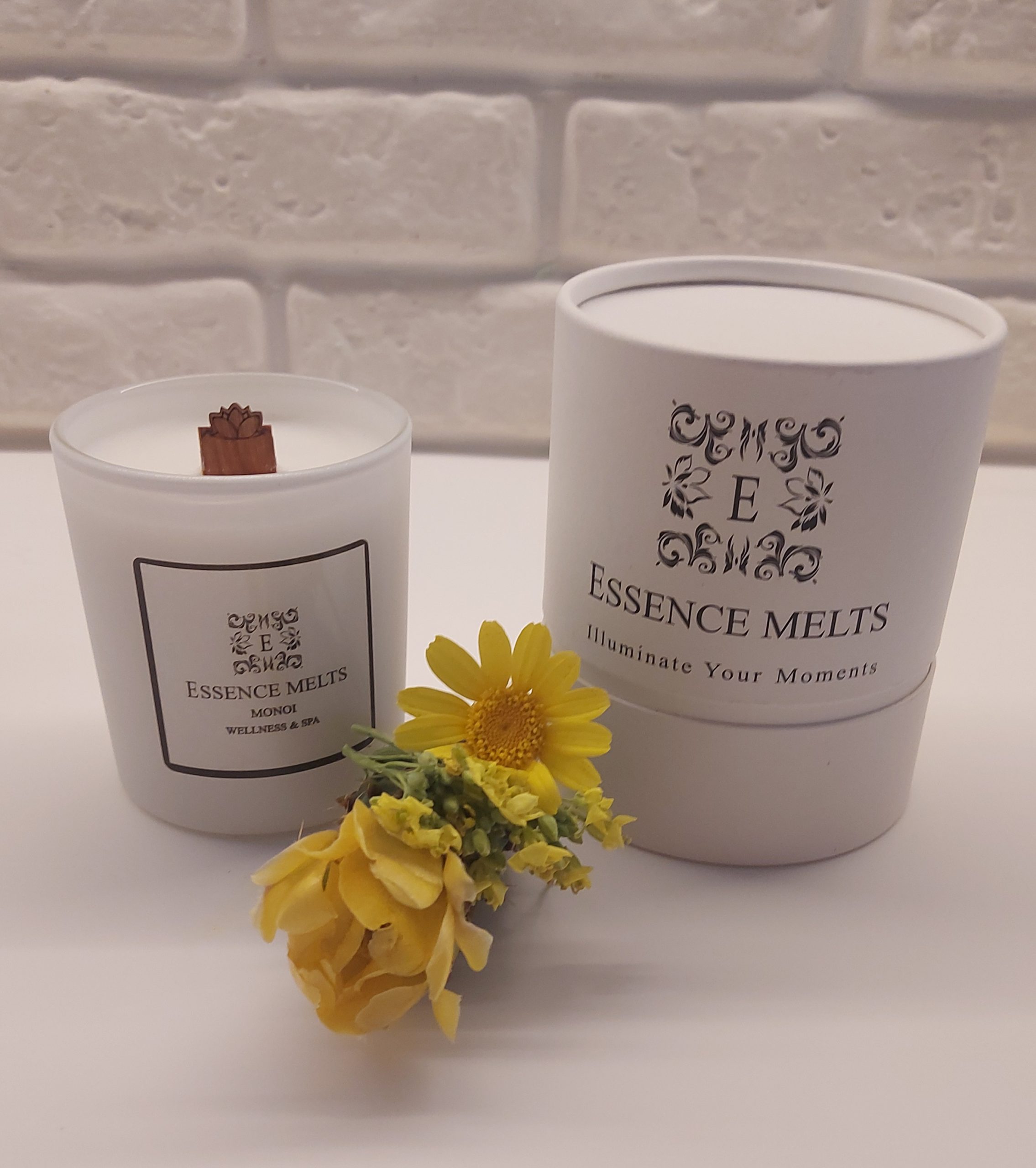 Monoi scented candle in a white ceramic container with a cherry wood wick, surrounded by tropical flowers and coconut. Spa candles