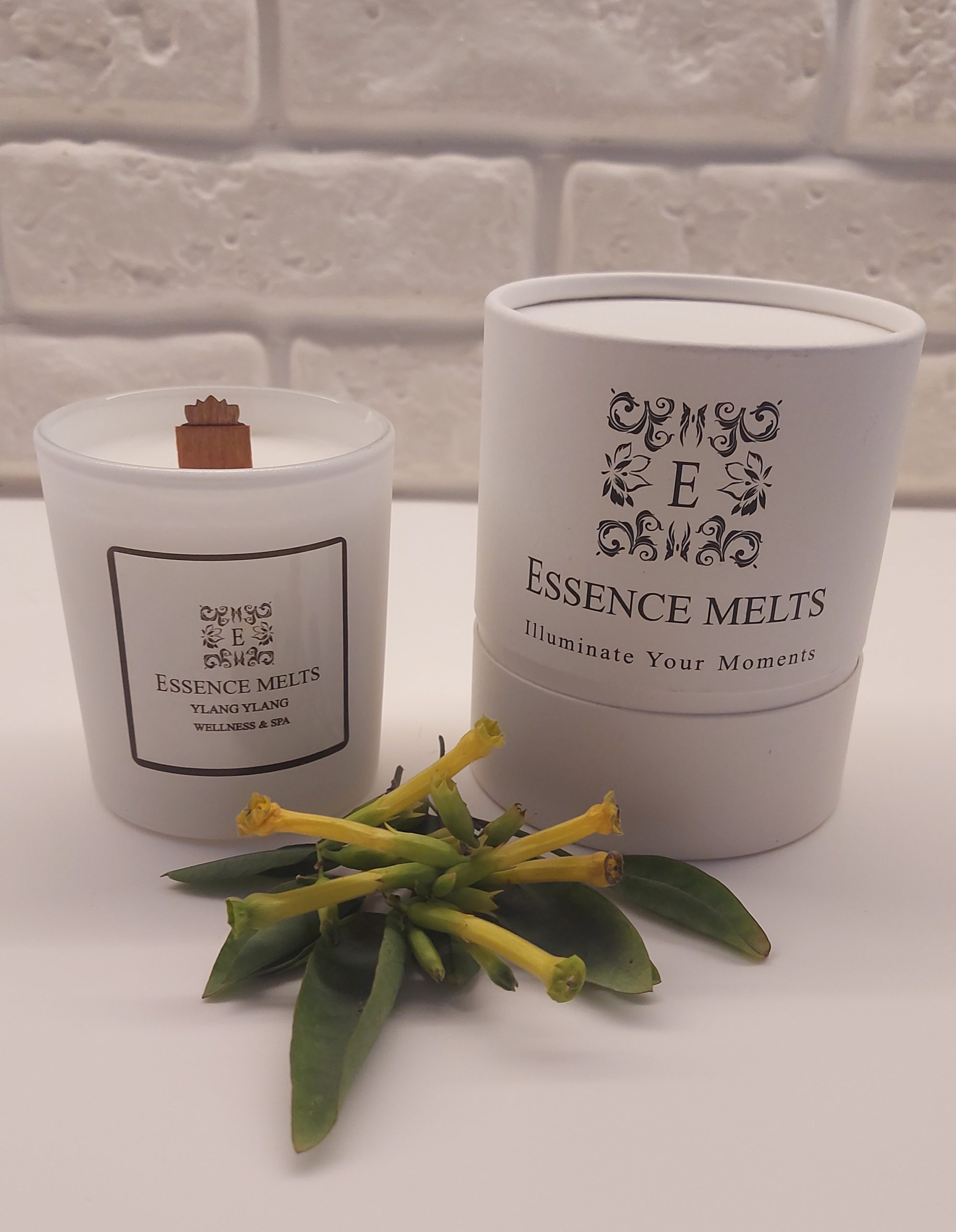 Ylang Ylang Spa Candle burning in a white glass container with a soft glowing flame. a exotic, floral scent. Spa Candles