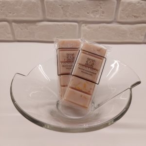 Orange Sandalwood wax melt snap bar wrapped in clear cellophane with Essence Melts logo, placed on a neutral-toned background