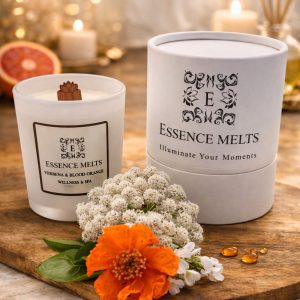 White glass candle labeled Verbena & Blood Orange, placed on a rustic wooden surface with a blurred natural background. Spa Candles