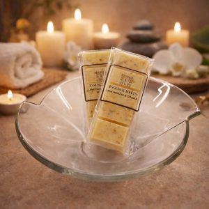 Patchouli & Amber scented wax melts by Essence Melts displayed in a glass bowl with a cozy spa background featuring candles, stones, and warm ambient lighting.