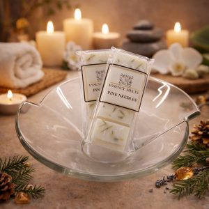 Pine Needles scented wax melts by Essence Melts displayed in a glass bowl with a cozy spa-style background featuring candles, pinecones, and evergreen branches.
