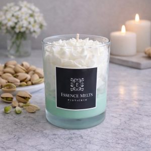 Pistachio-scented candle in a glass jar with creamy wax and a warm nutty tone, styled against a light neutral background. Dessert candles