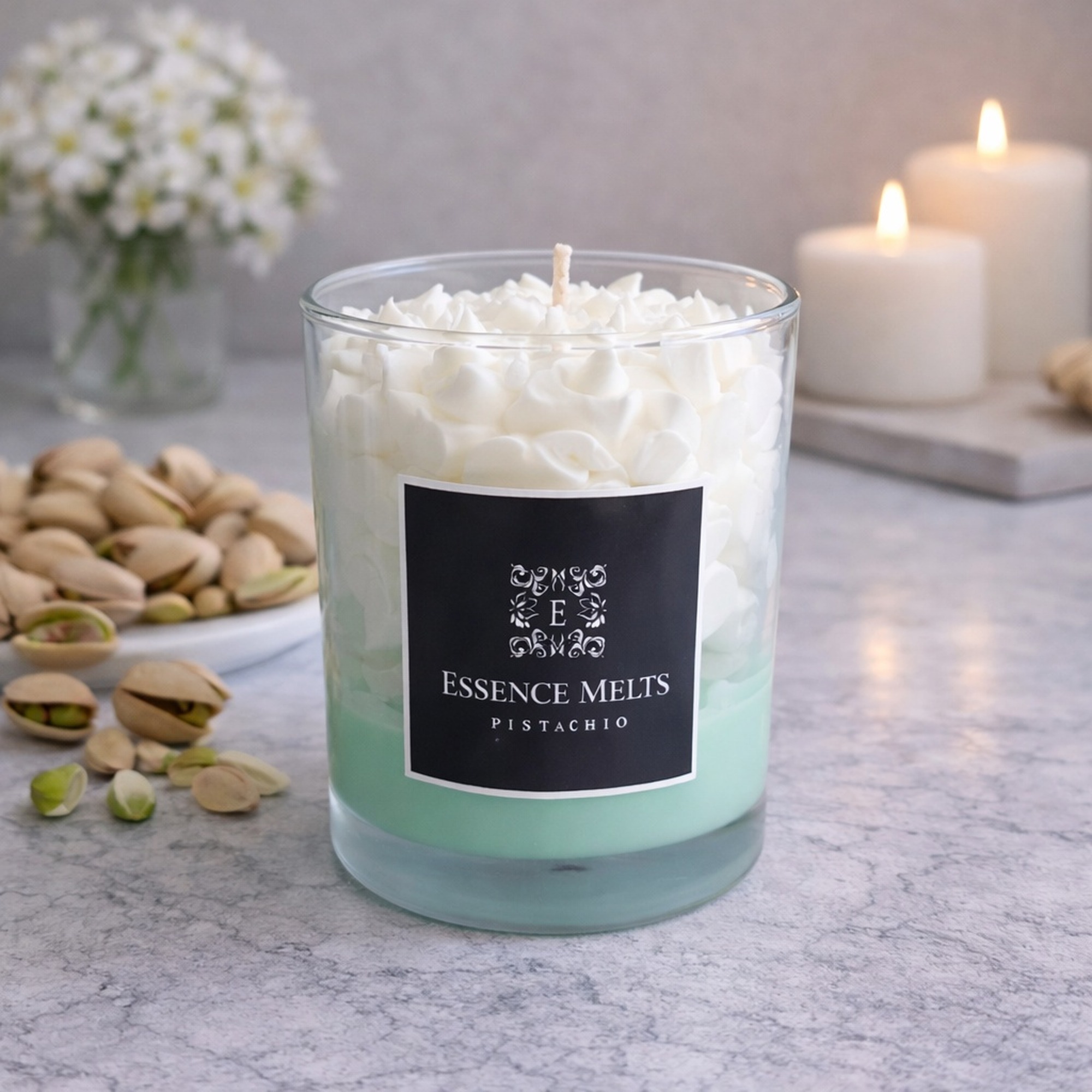 Pistachio-scented candle in a glass jar with creamy wax and a warm nutty tone, styled against a light neutral background. Dessert candles