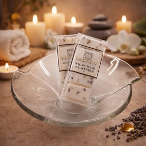 White Musk & Lavender scented wax melts by Essence Melts displayed in a glass bowl with a cozy spa background featuring candles, stacked stones, and soft ambient lighting.