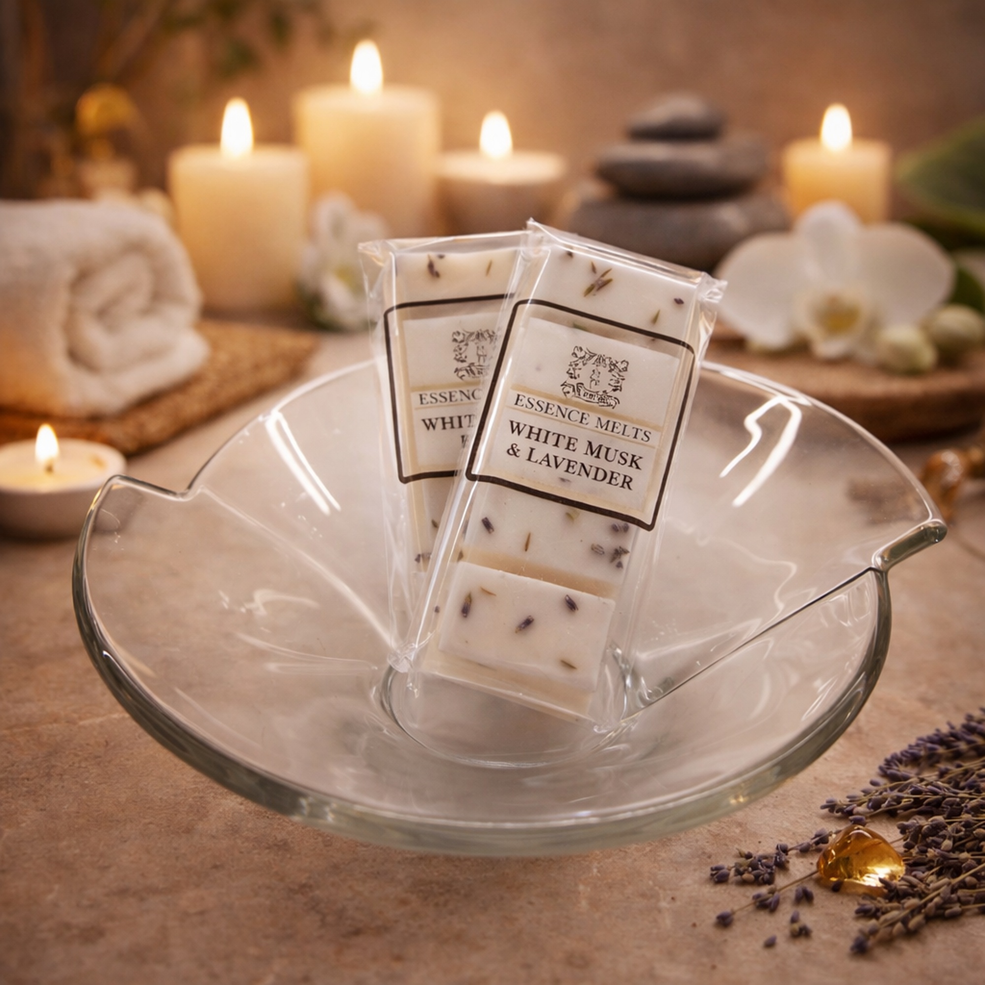 White Musk & Lavender scented wax melts by Essence Melts displayed in a glass bowl with a cozy spa background featuring candles, stacked stones, and soft ambient lighting.