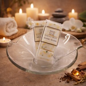 Ylang Ylang scented wax melts by Essence Melts displayed in a glass bowl with a warm spa background featuring candles, stacked stones, and soft ambient lighting.