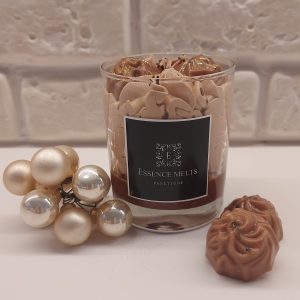 Panettone dessert candle in glass jar with whipped brown wax topping and sprinkles, beside two matching wax melts and decorative ornaments. Dessert candles