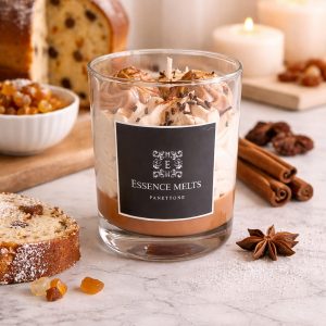 Panettone dessert candle in glass jar with whipped brown wax topping and sprinkles, beside two matching wax melts and decorative ornaments. Dessert candles