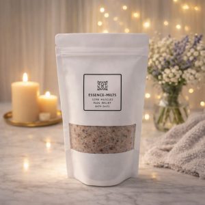 Essence Melts Sore Muscles and Pain Relief Bath Salts in white pouch with pink and mineral salt blend on cozy spa background