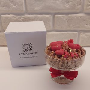 Chocolate Love Candle with gold flakes in a glass dessert-style vessel next to a white Essence Melts gift box, topped with red heart-shaped wax pieces and whipped chocolate-colored wax.