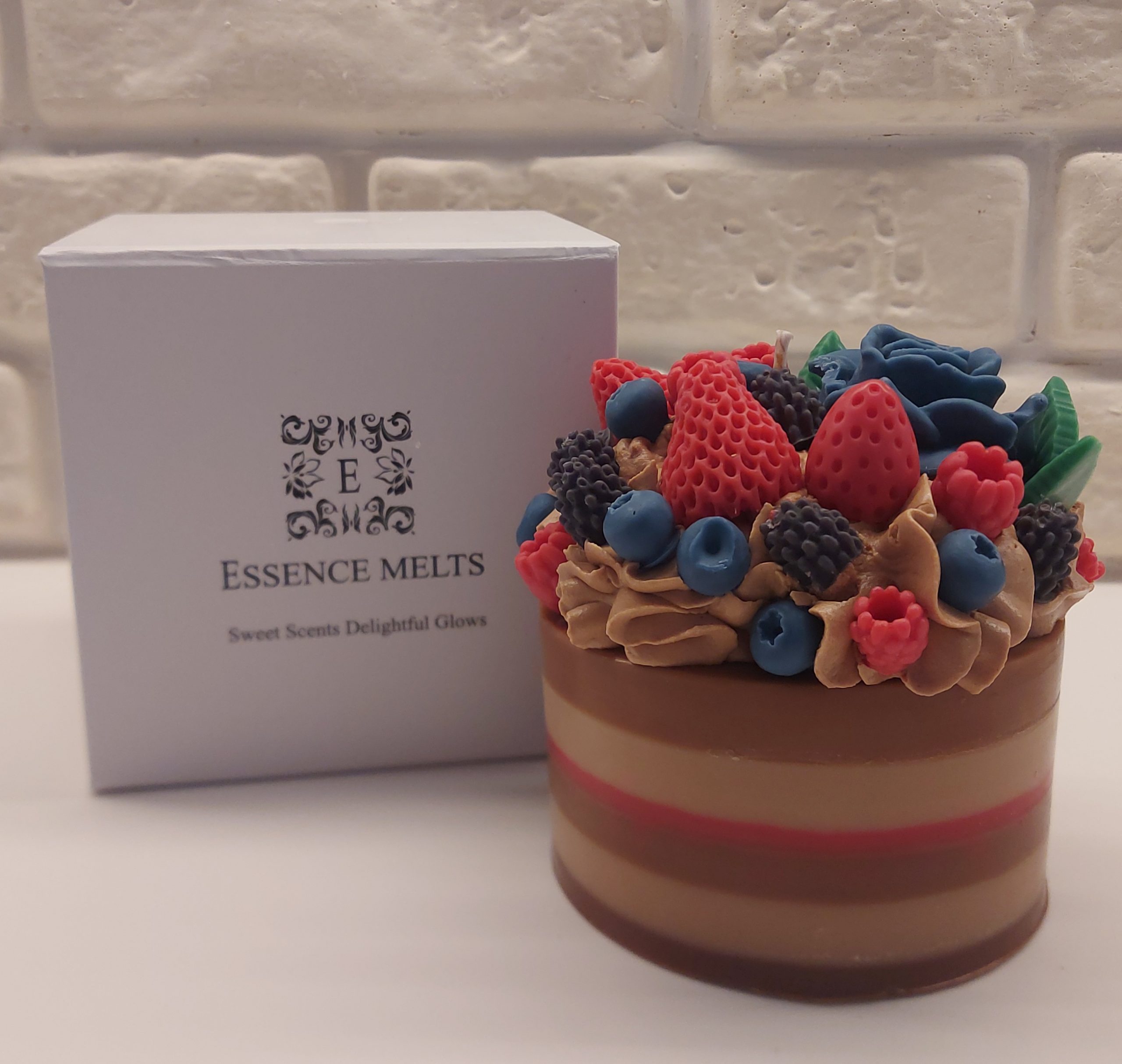 Decorative soy wax cake candle topped with colorful wax berries and floral details, placed beside a white Essence Melts box.