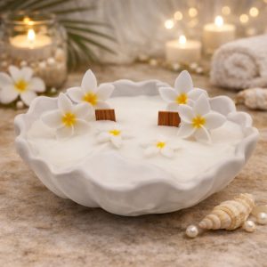 Seashell Spa candle in a white seashell-shaped container with natural beige wax, two cherry wood wicks softly glowing, and delicate wax flowers on top. Spa candles