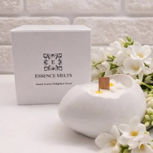 Monoi Egg 1 Candle in an elegant white cracked-egg-shaped vessel with floral wax accents and a cherry wood wick, placed beside a branded Essence Melts box.