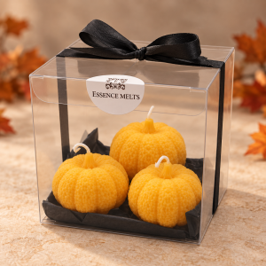 Three orange textured pumpkin candles in a clear gift box with black tissue paper, a black satin bow and Essence Melts label.