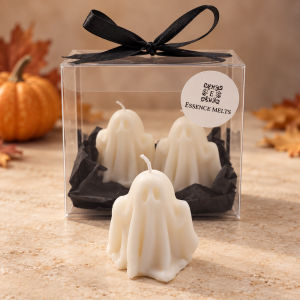 White ghost-shaped Little Boo candles with a clear Essence Melts gift box, black ribbon and autumn pumpkin background.