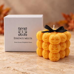 Spooky Smiles candle with three rows of orange jack-o’-lantern faces and a black bow, beside a white Essence Melts box.