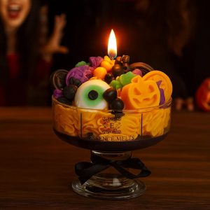 A colorful Halloween candle in a glass dessert bowl, topped with whipped wax and spooky wax decorations including pumpkins, eyeballs, candy shapes, and bats.