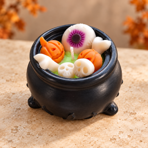 Candy Cauldron candle in a black vessel with green wax, orange pumpkins, ivory skulls and a purple eyeball decoration.